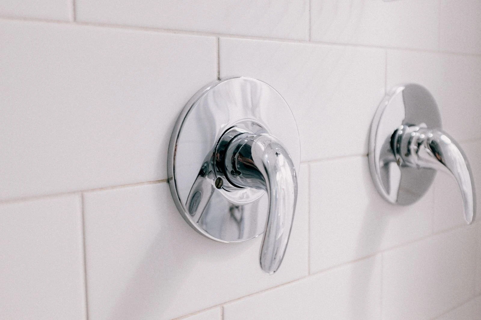 Close-up of chrome handles on a white tiled bathroom wall, capturing elegance and hygiene