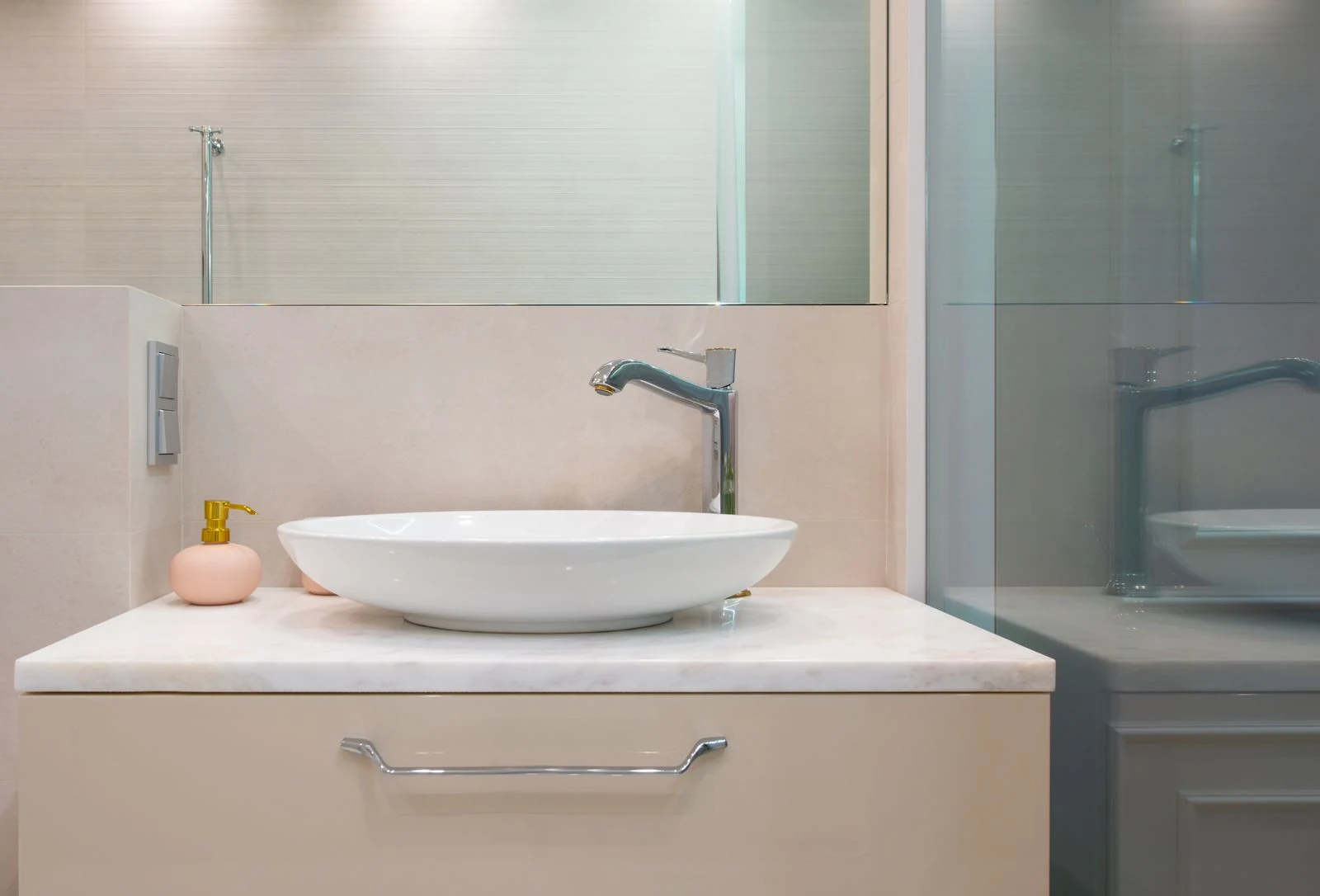Interior of light modern washroom with sink and faucet on cabinet with decorative objects under mirror on wall next to glass wall