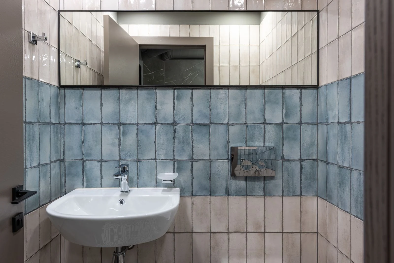 Interior of modern restroom with ceramic white sink and mirror hanging on white and blue tiled wall