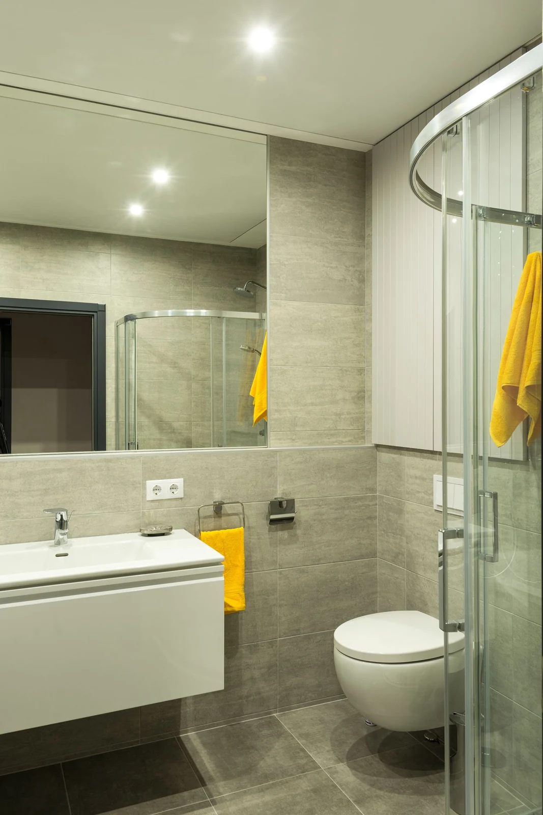 Sleek modern bathroom with a shower, sink, and toilet, featuring yellow towels for a pop of color